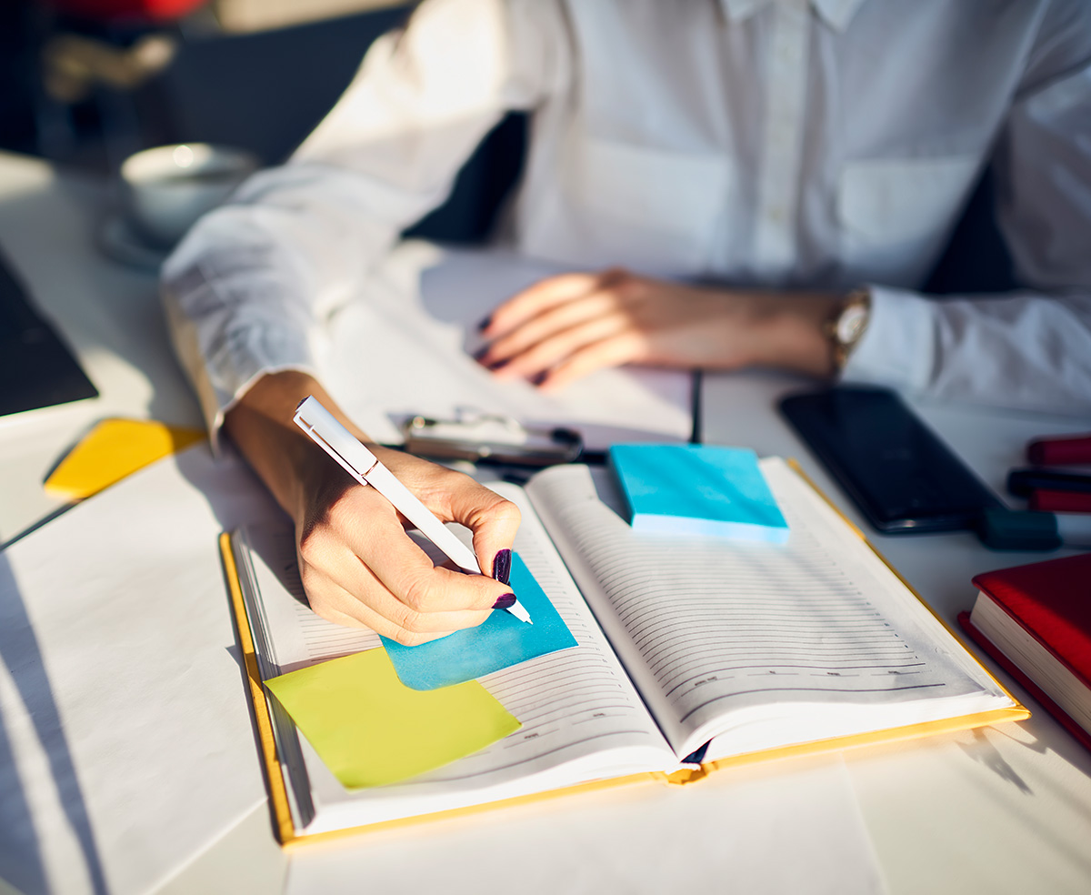 female in white lab coat writing in book with sticky notes