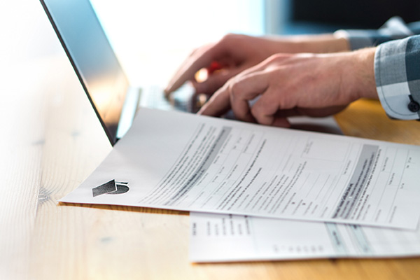 hands typing on computer next to papers