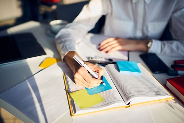 female in white lab coat writing in book with sticky notes