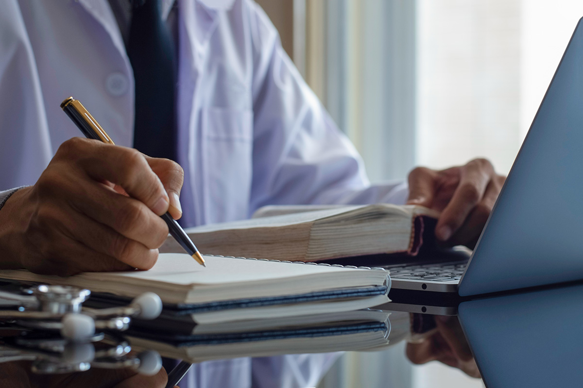 doctor writing a note next to laptop