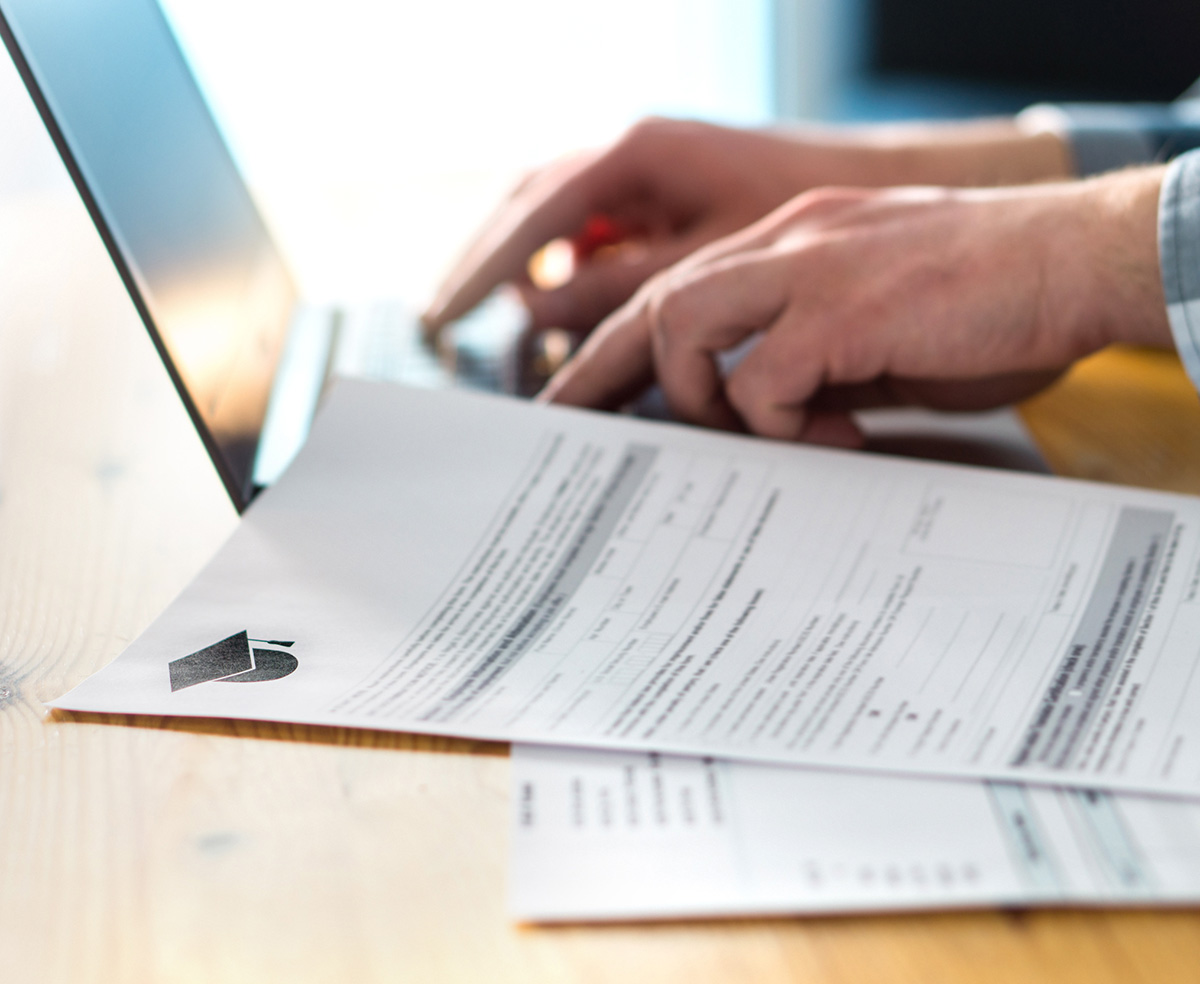 hands typing on computer next to papers